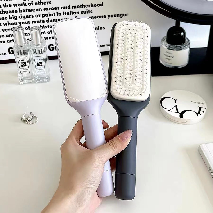 Two hairbrushes, one white and one gray, held by a hand on a blurred background with products.